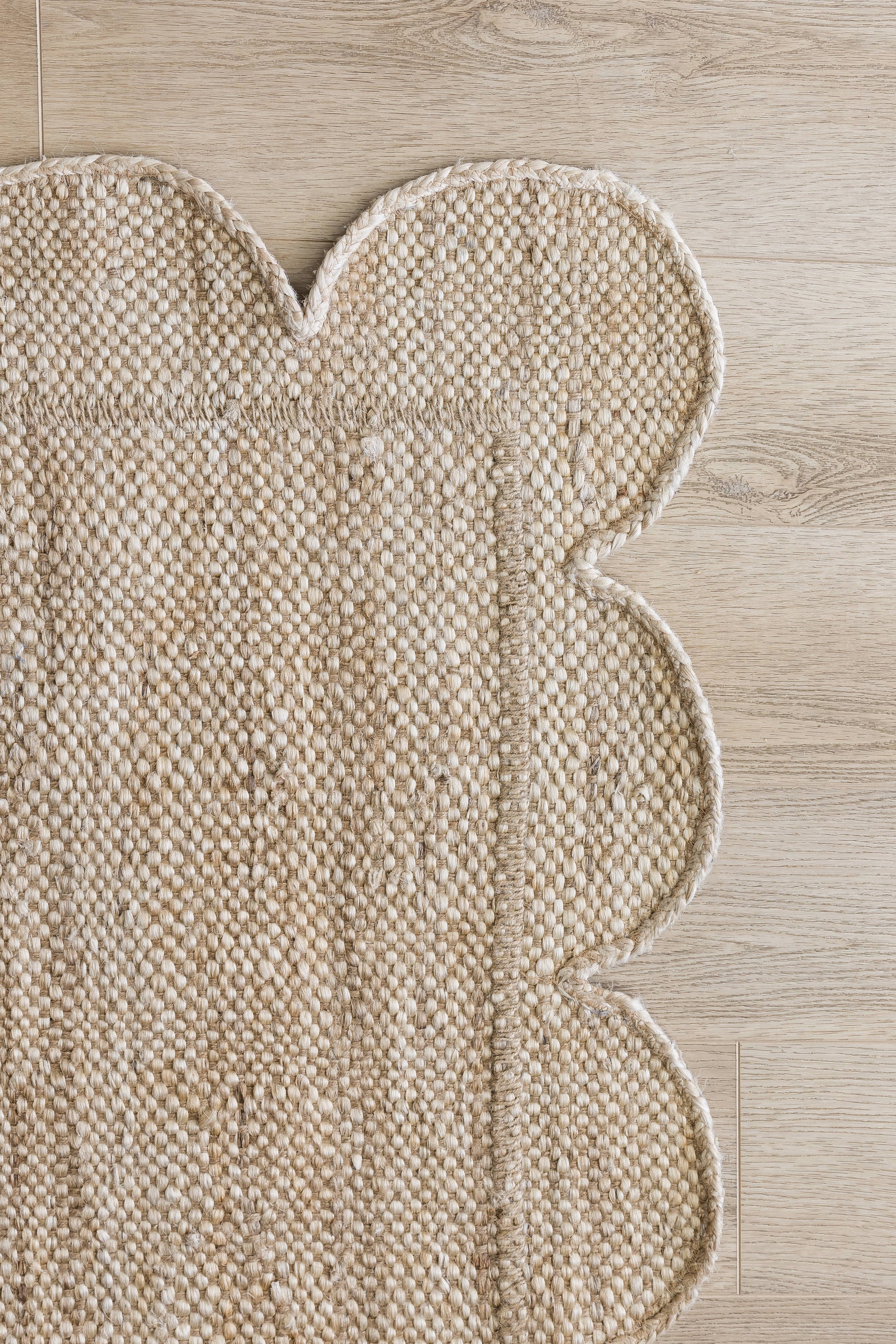 Natural beige woven rug with a scalloped edge on light wood floor; textured looped fibers.