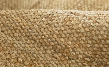Close-up of natural beige jute fabric weave; burlap-like texture visible on a rug runner.