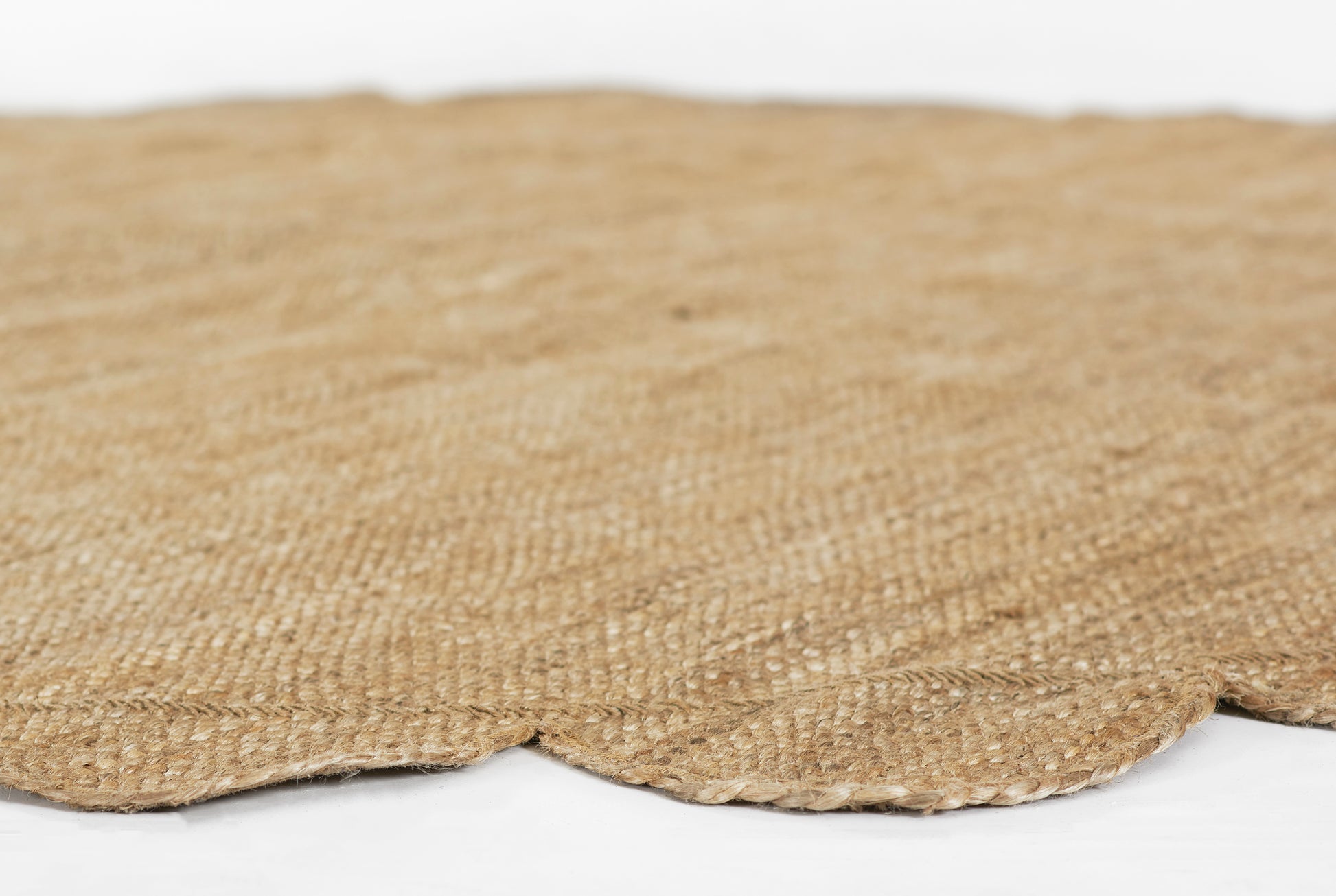 Natural jute round rug with scalloped edge & textured woven fibers in beige.