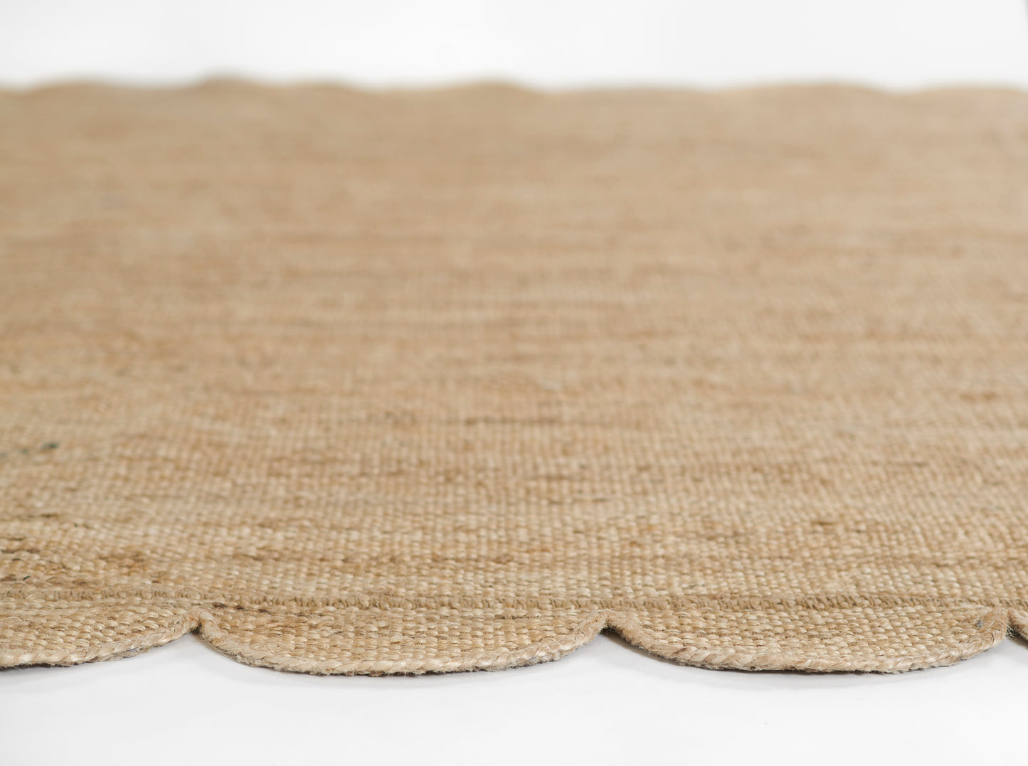 Natural jute rug in warm beige with scalloped edge; rustic woven floor mat.