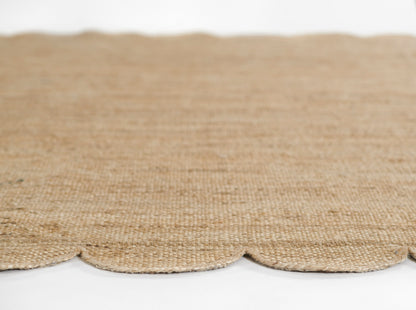 Natural jute rug in warm beige with scalloped edge; rustic woven floor mat.
