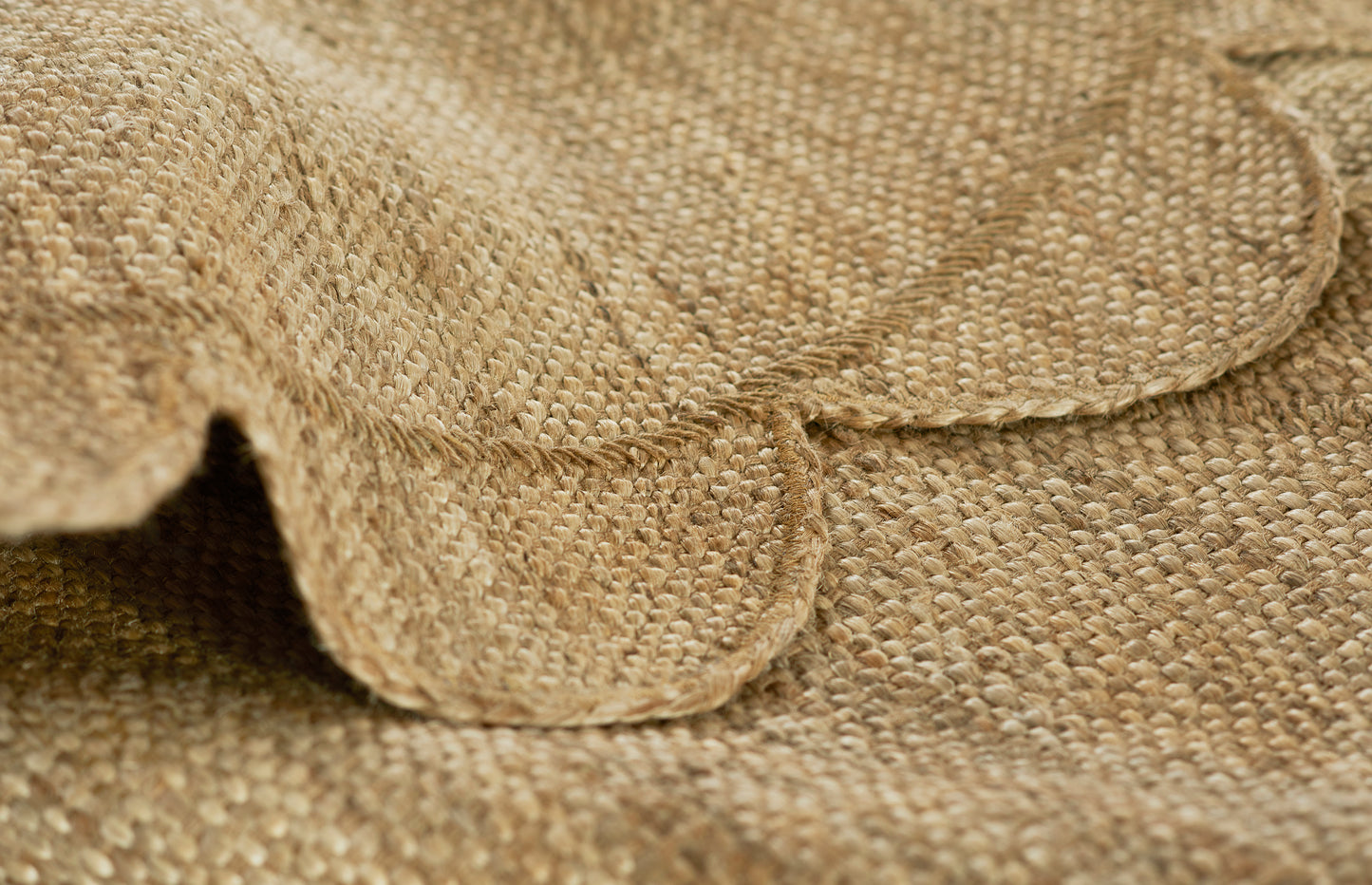 Natural burlap fabric close-up of a round rug: woven jute texture with folded edge in warm beige-brown.
