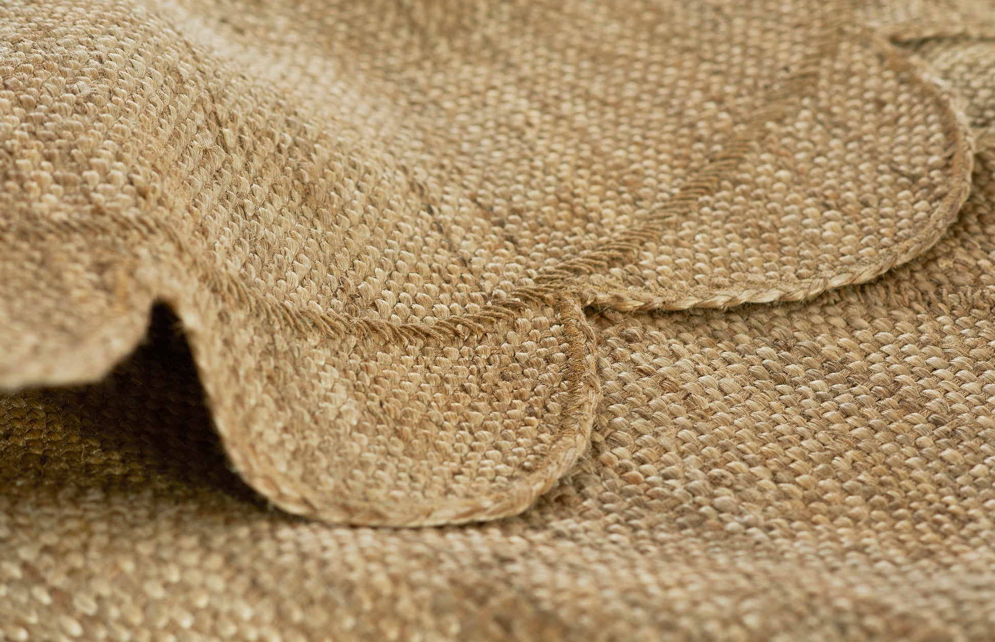 Natural burlap fabric close-up of a round rug: woven jute texture with folded edge in warm beige-brown.