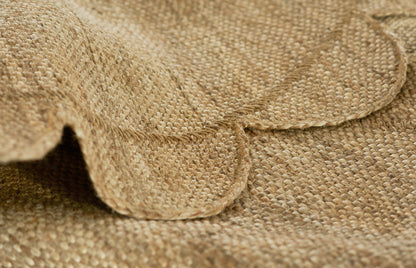 Natural burlap fabric close-up of a round rug: woven jute texture with folded edge in warm beige-brown.