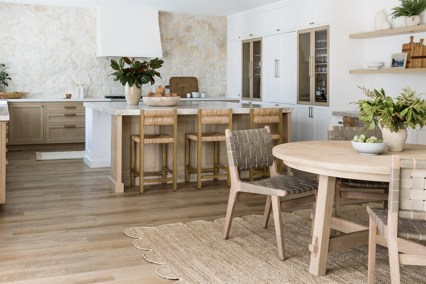 8' x 11' rug in a bright kitchen-dining space with white cabinets, light wood floors, an island with bar stools, and a round dining table with plants.