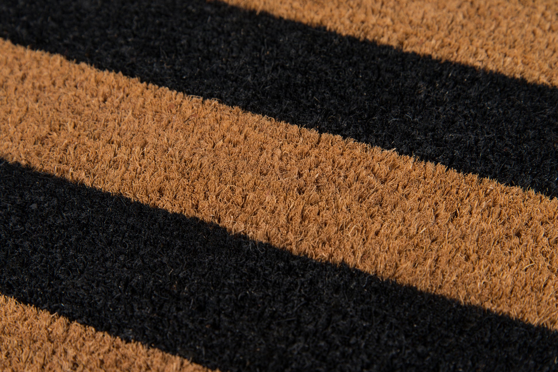 Diagonal brown and black striped coir doormat with textured fibers for front-door use.
