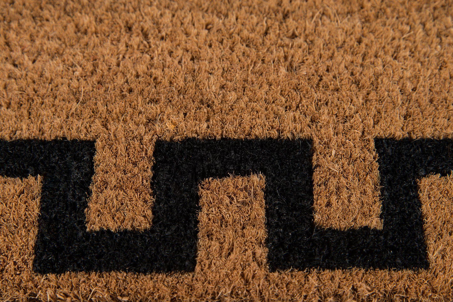 Natural brown coir rug with a black Greek-key geometric pattern; coarse fibrous texture for entrance use.