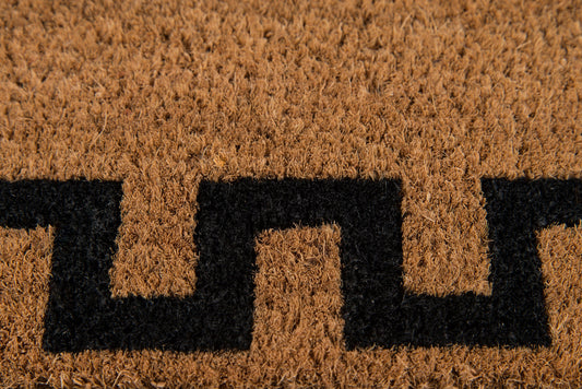 Natural brown coir rug with a black Greek-key geometric pattern; coarse fibrous texture for entrance use.