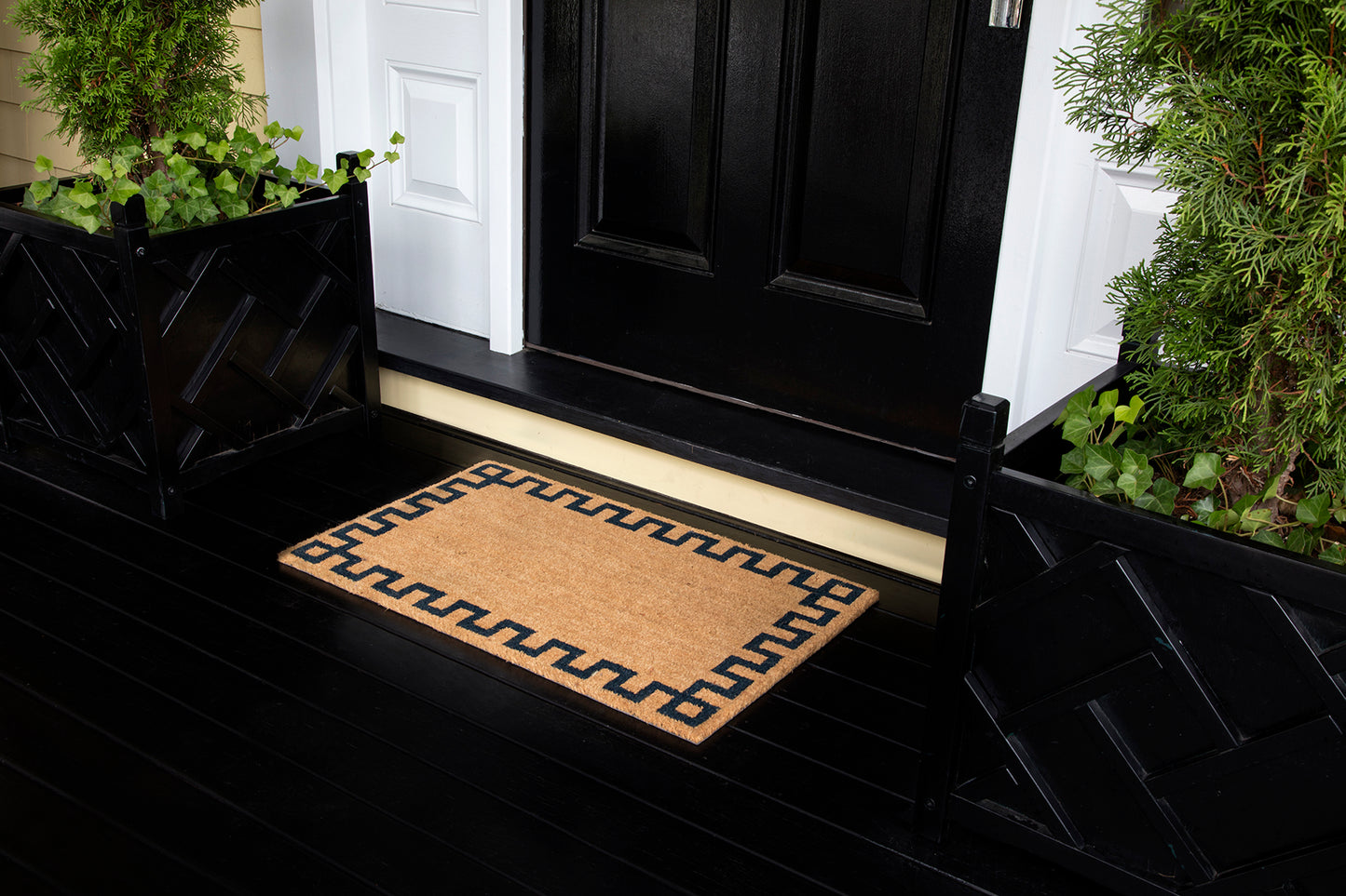 Natural coir doormat with a black Greek-key border on a black porch in front of a black front door.