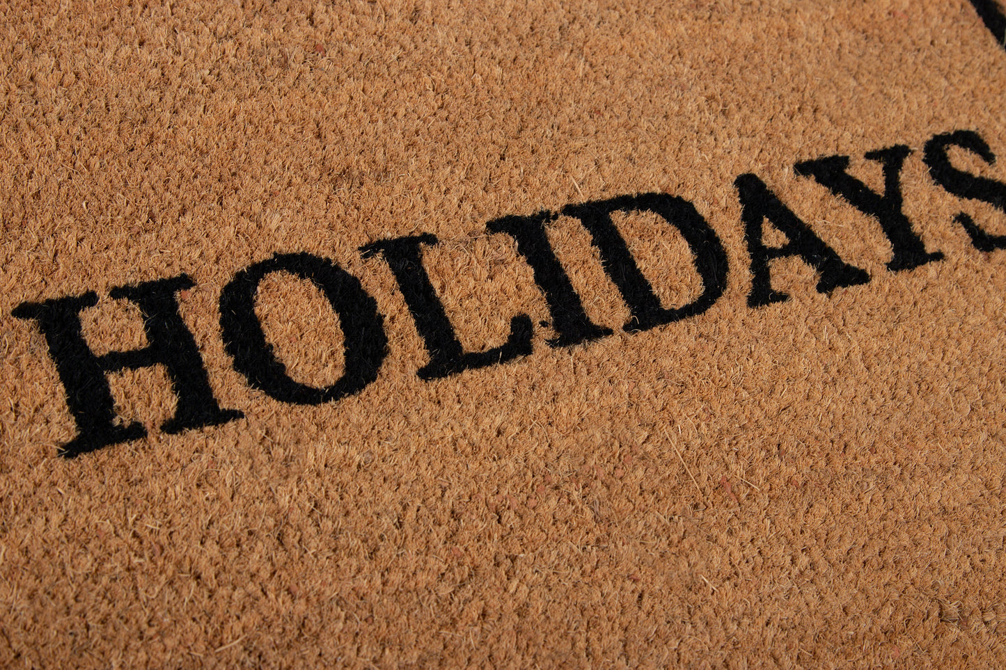 Coir doormat in tan with bold black HOLIDAYS lettering; textured fiber surface.