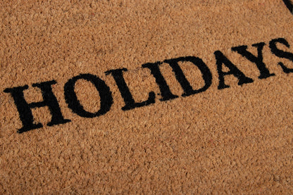 Coir doormat in tan with bold black HOLIDAYS lettering; textured fiber surface.