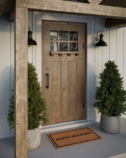 Rustic wood front door with grid window, black hardware, flanked by potted evergreens; siding and Happy Holidays doormat.