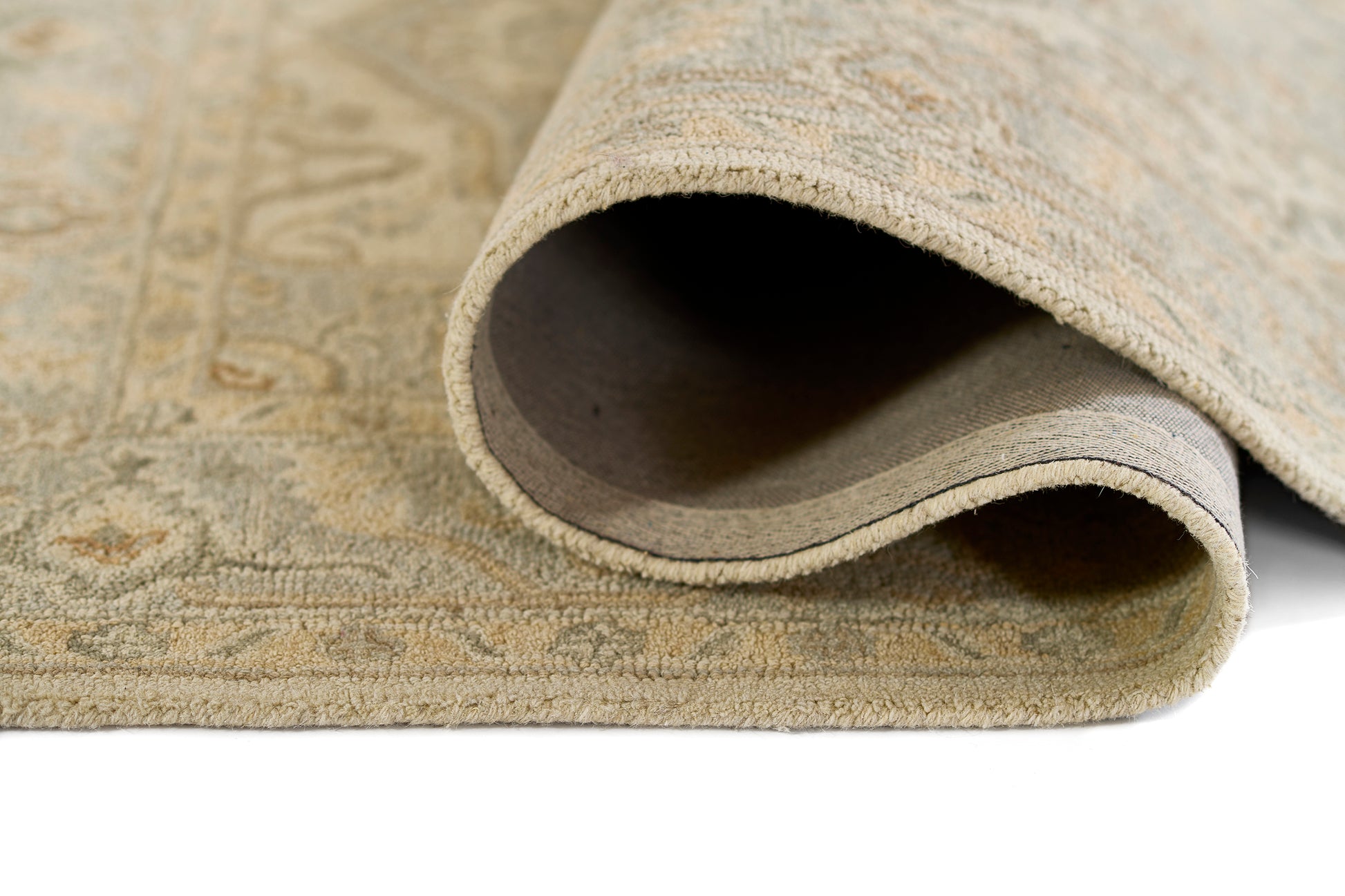 Beige patterned area rug with plush pile, curled edge exposing soft underside and subtle damask design.