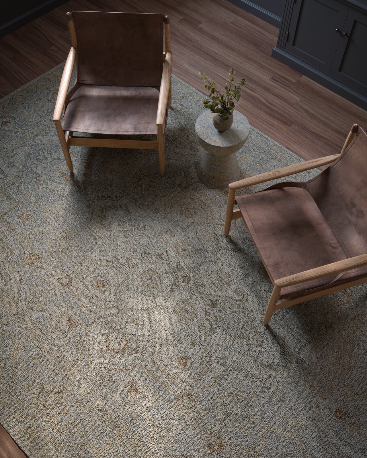 Two mid-century brown leather lounge chairs with light wood frames around a round side table with a plant on a patterned rug.