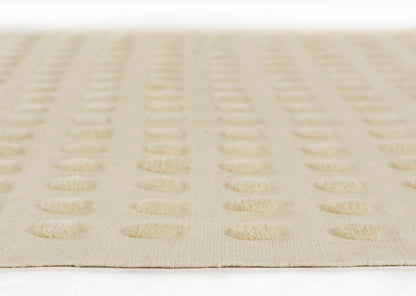 Beige woven rug with raised circular dot pattern in subtle rows, soft neutral home decor.