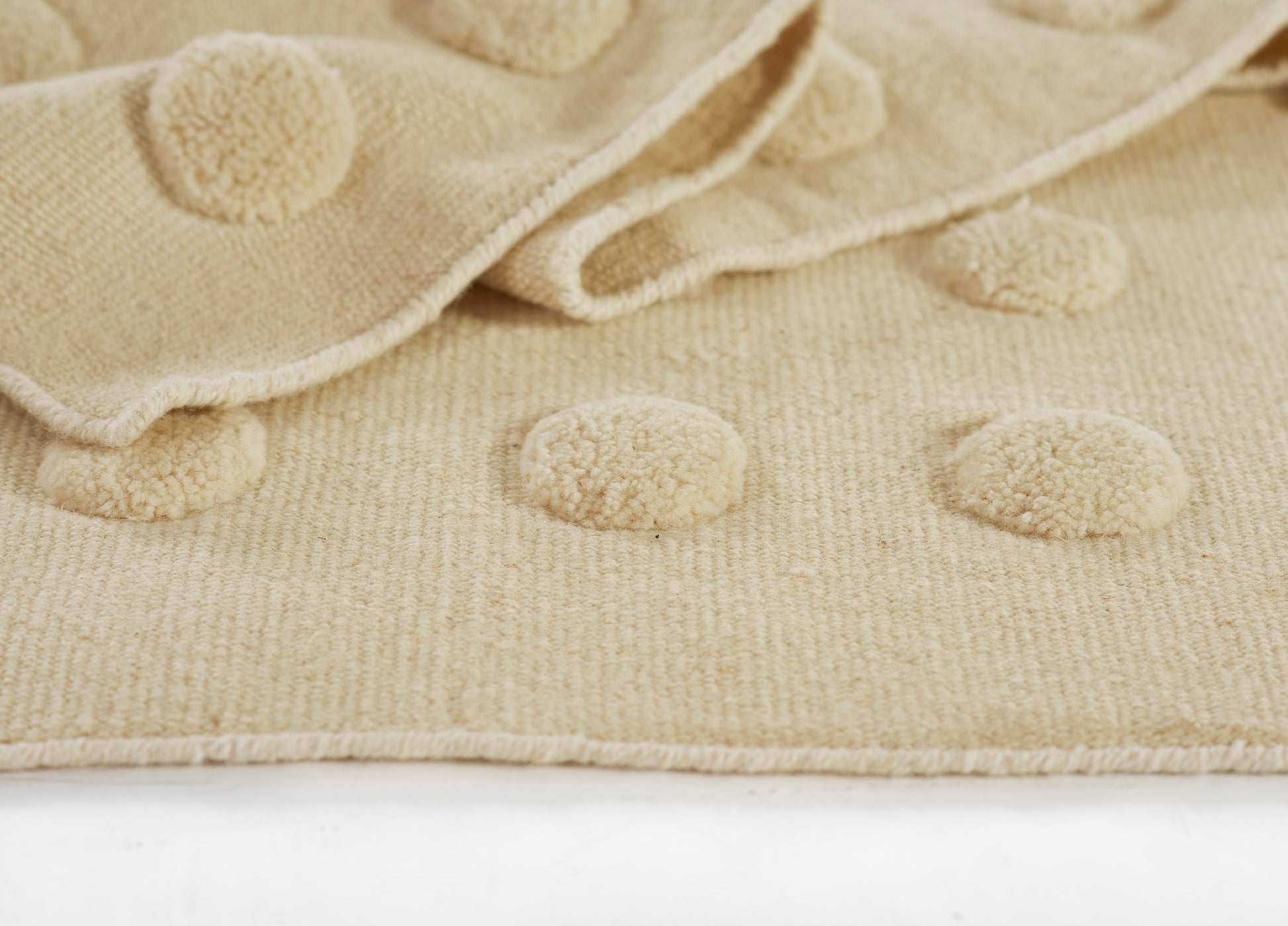 Beige boucle knit rug with raised round pom-pom dots; soft, cozy surface for living room or nursery (5' x 8').