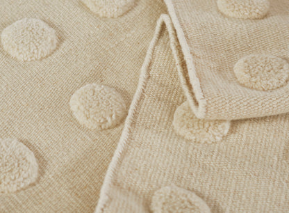 Beige towel with raised pom-pom dot texture, soft terry, folded edge, cozy bath linen.