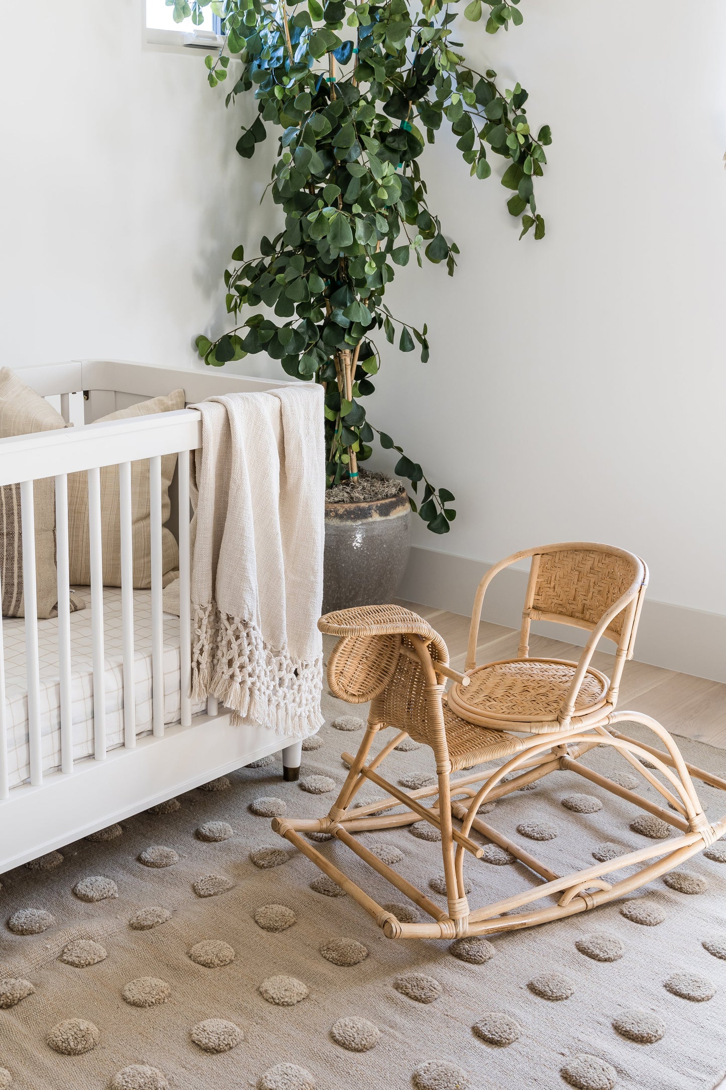 Natural rattan rocking chair with a woven seat, curved rockers in a light nursery near a large plant.