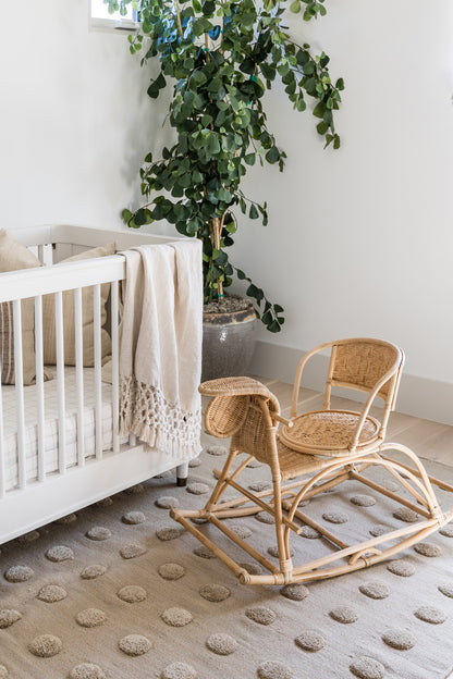 Natural rattan rocking chair with a woven seat, curved rockers in a light nursery near a large plant.
