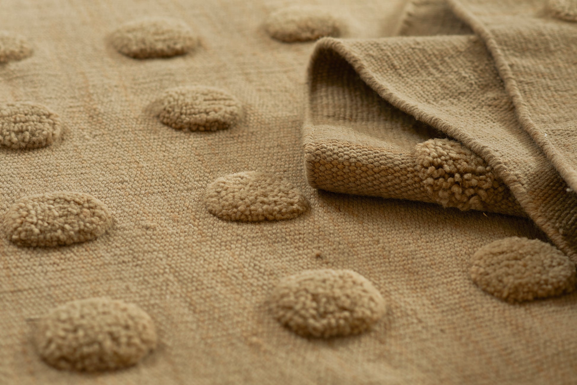 Taupe tufted rug with circular raised dots and soft woven texture; folded corner.