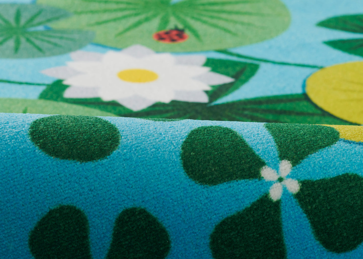 Blue rug with green lily pads and a white flower with yellow center; plush, vibrant tropical print.