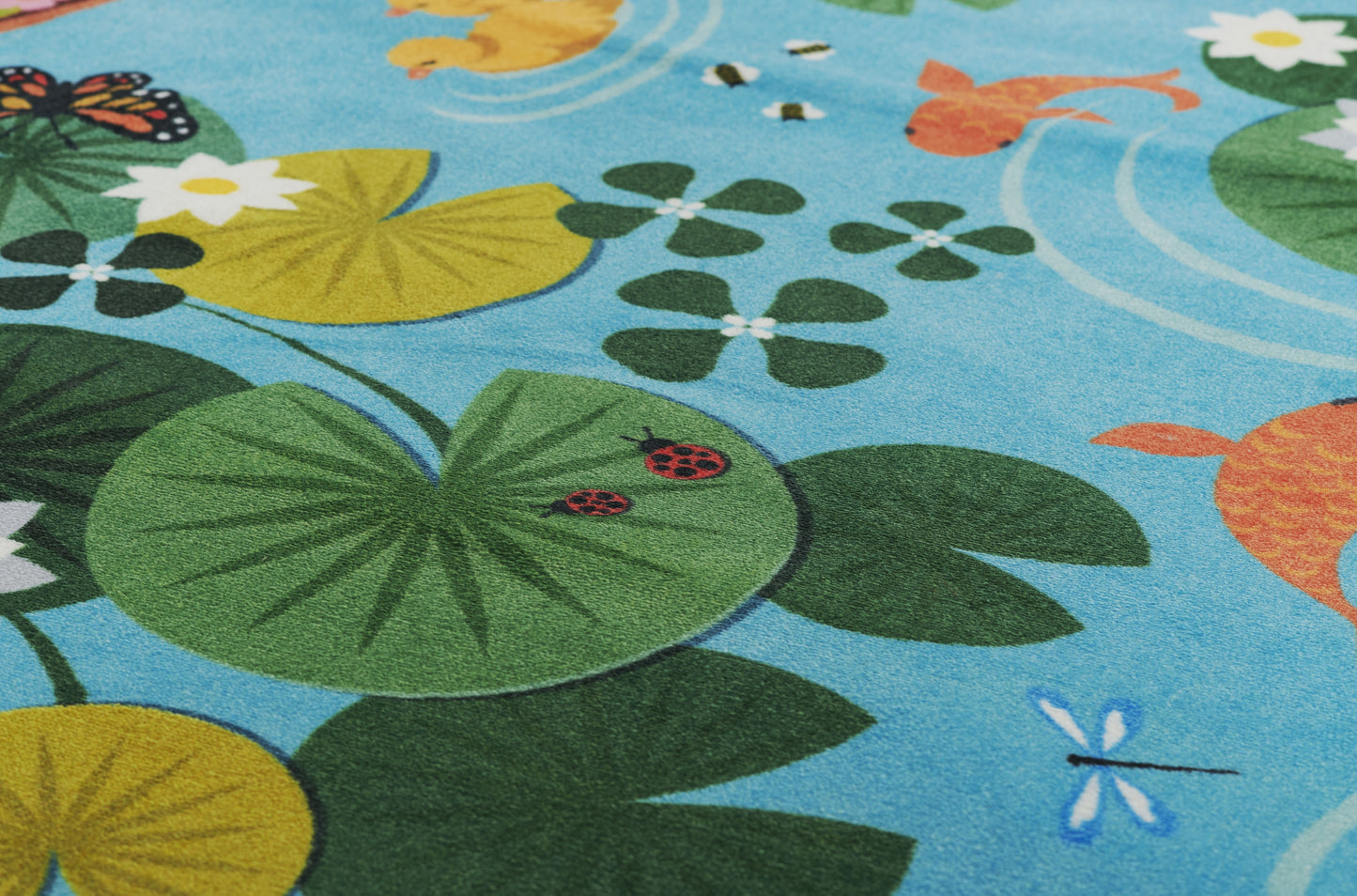 Blue kids play mat with green and yellow lily pads, orange fish, and dragonflies; soft textile rug for playroom decor.