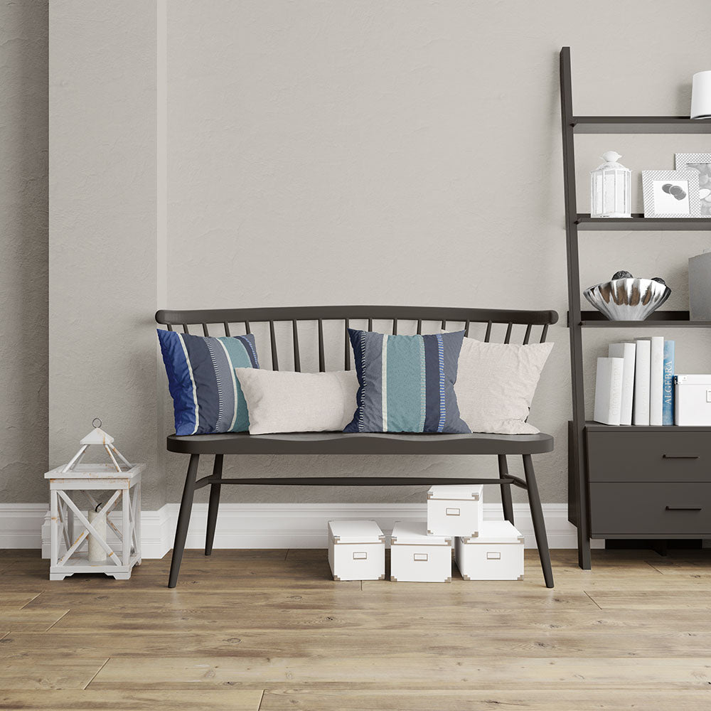 Moonlit Stroll Stripe fabric cushions in blue & gray stripes on a dark metal bench against a gray wall, beside a black shelving unit with books.