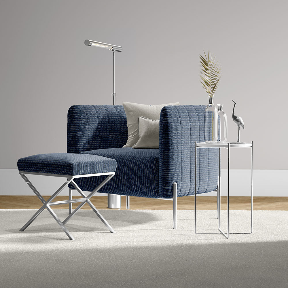 Navy blue textured armchair with matching ottoman and chrome legs, beside glass side table with vase and crane statue.