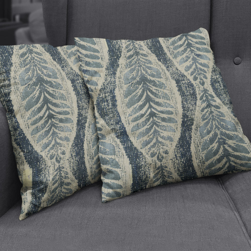 Two rectangular throw pillows in blue and cream with an indigo abstract botanical stripe pattern on a gray sofa.