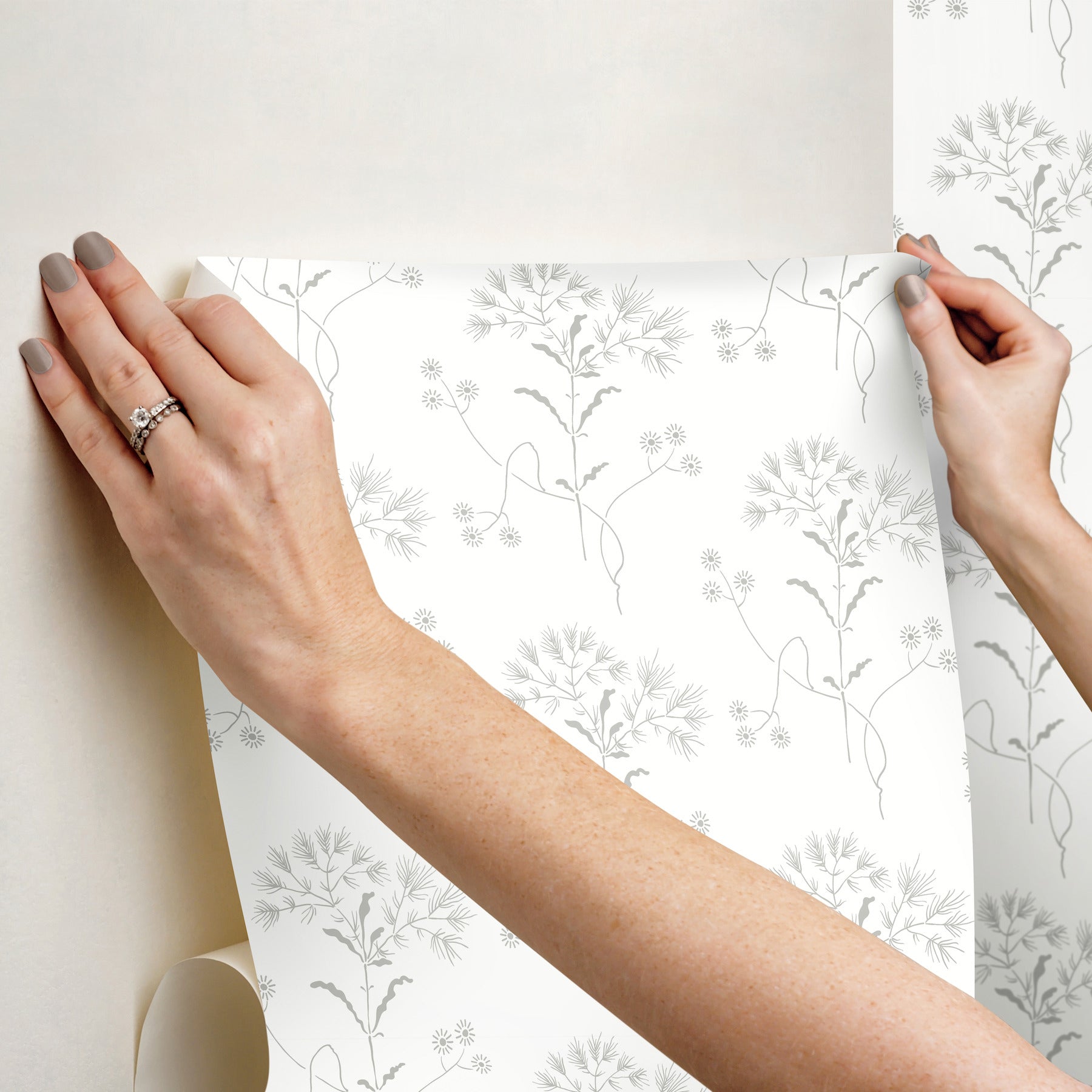 Hands apply a white wallpaper sheet with light grey botanical stems and tiny flowers.