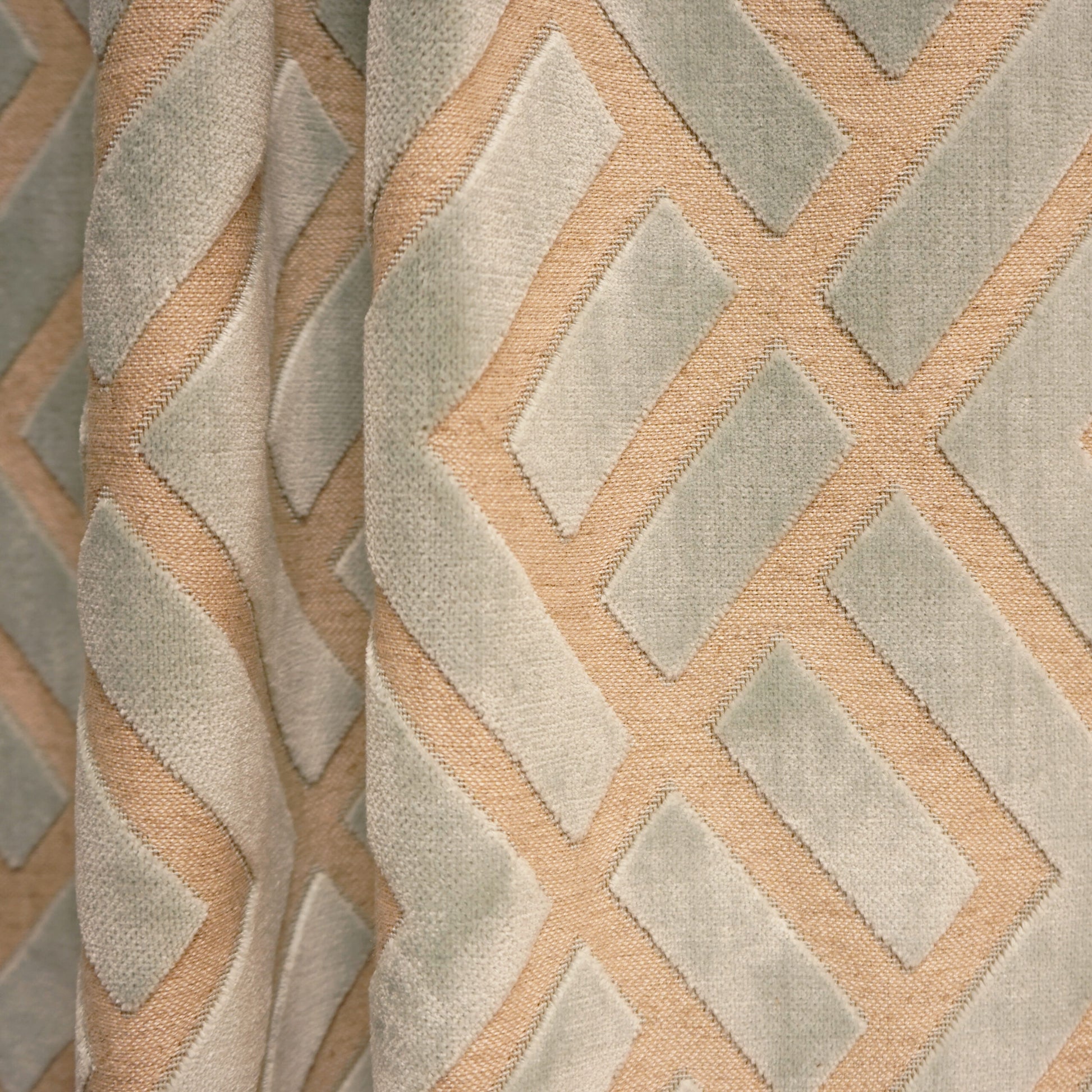 Textured curtain fabric with geometric blue and creme diamond lattice on a pale beige background, softly folded.