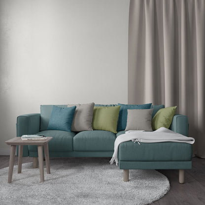 Teal sectional sofa with chaise in living room, multicolored cushions, grey throw, wooden side table with magazines.