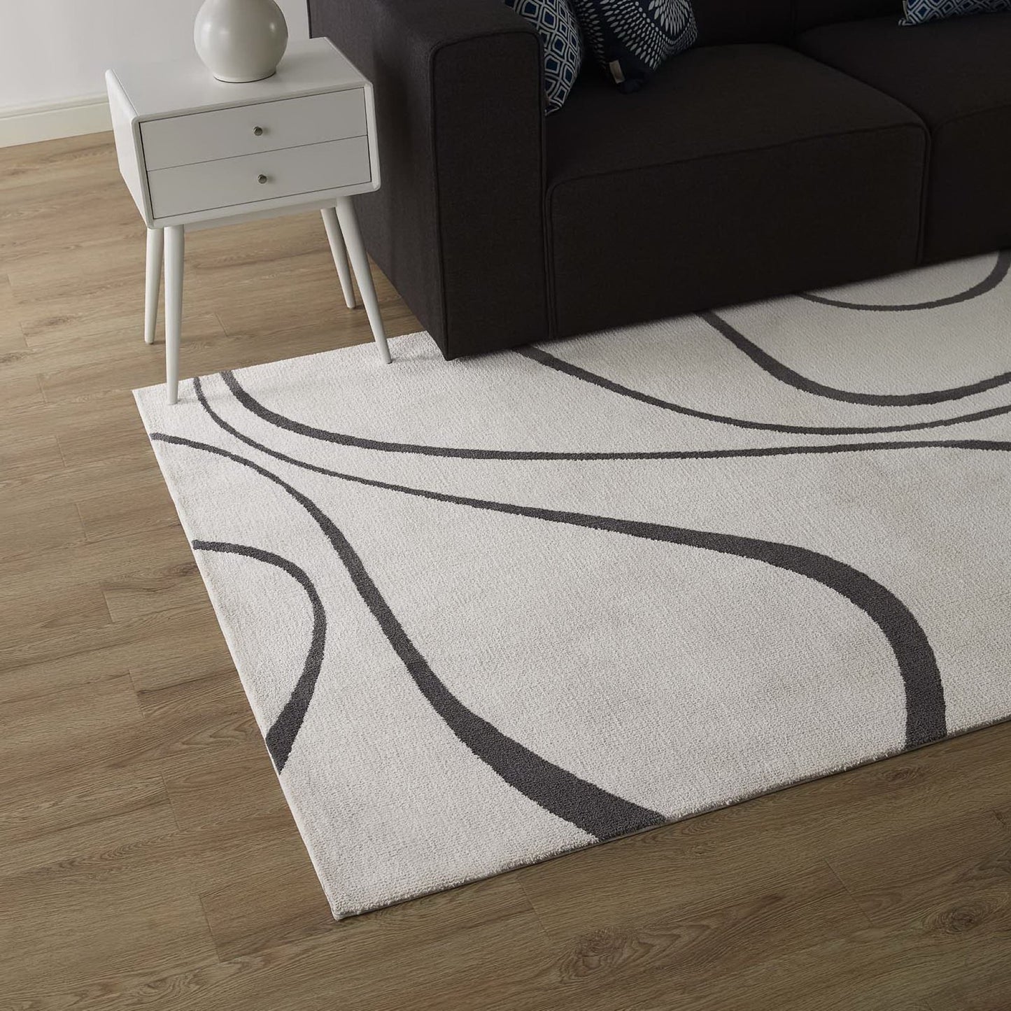 Cream area rug with sweeping charcoal curves, paired with a white two-drawer side table and a dark sofa