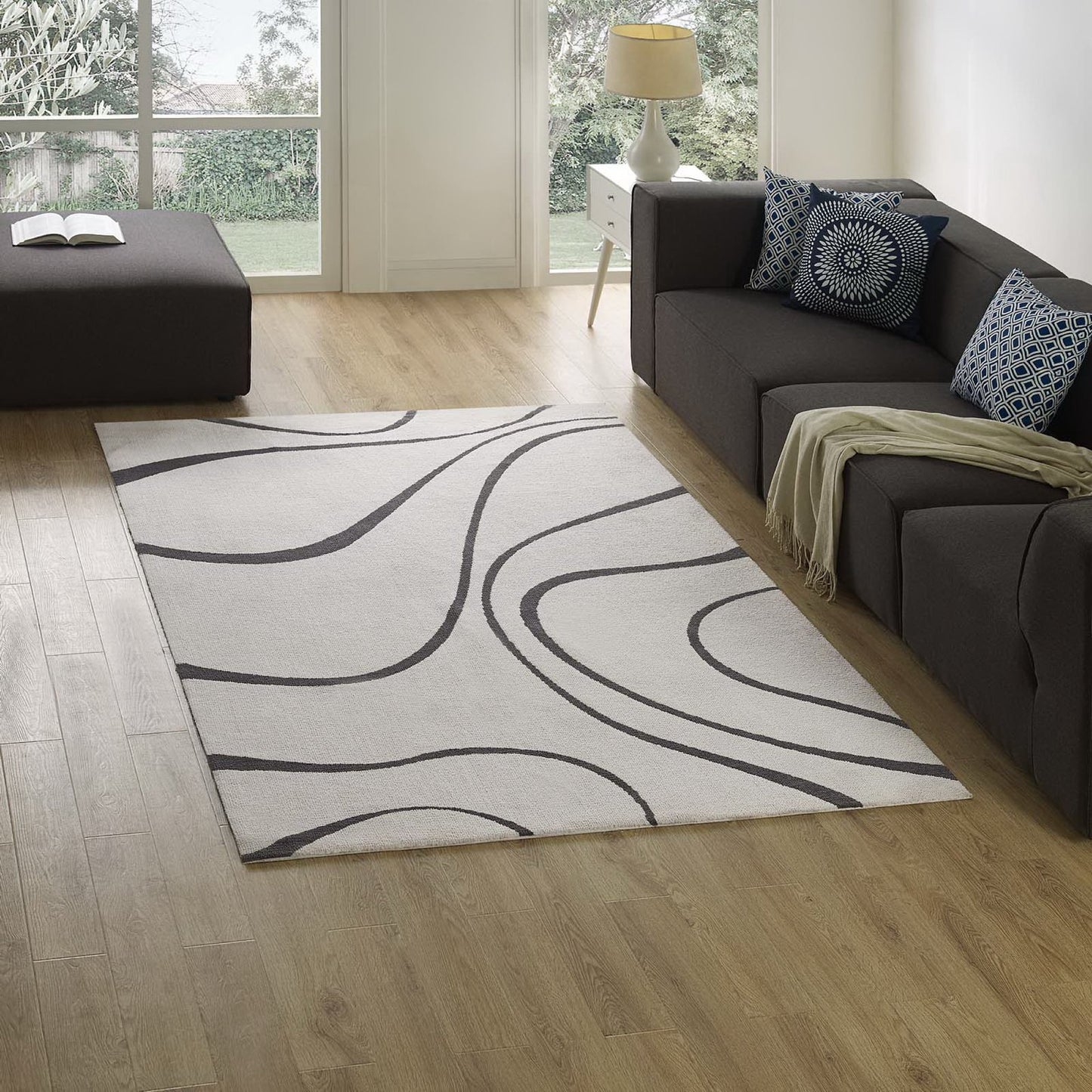 Ivory & charcoal abstract swirl area rug under a dark gray sectional sofa with blue patterned cushions.
