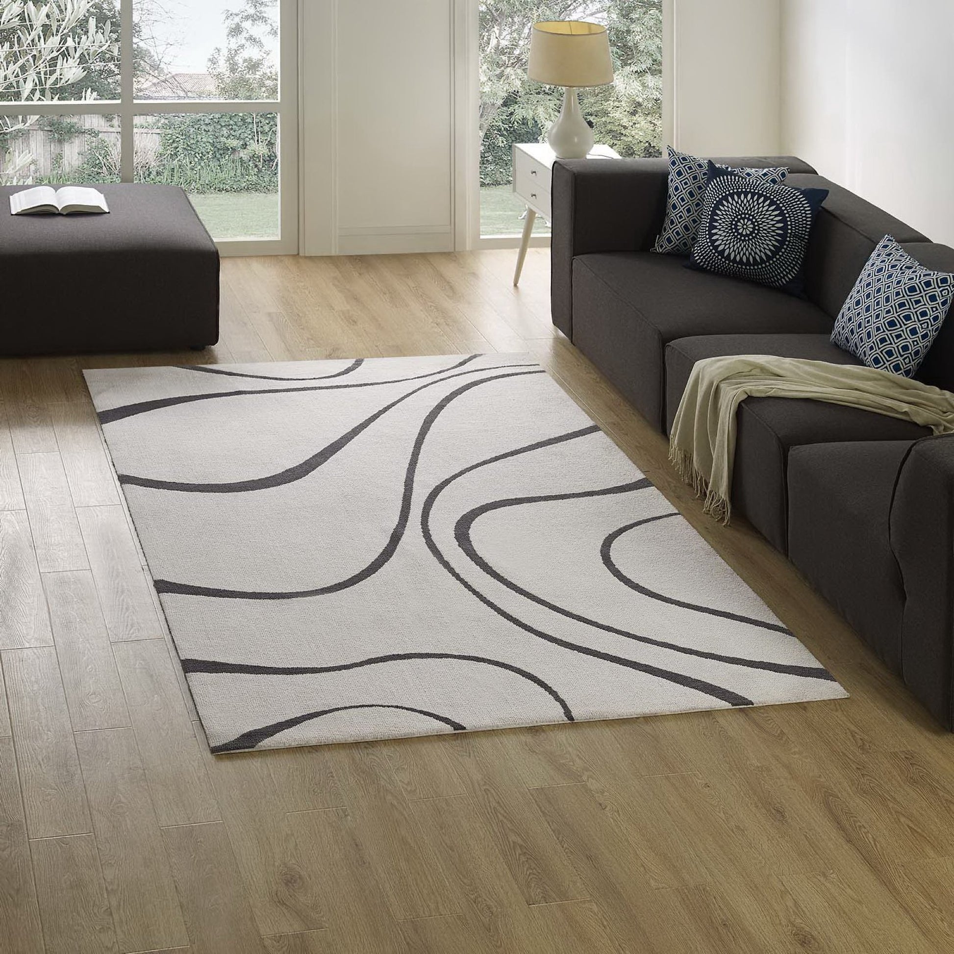 Ivory & charcoal abstract swirl area rug under a dark gray sectional sofa with blue patterned cushions.