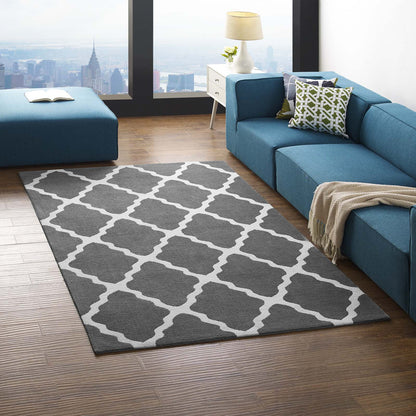 Grey area rug with white trellis pattern on wood floors; blue sectional sofa, pillows, and city skyline visible.