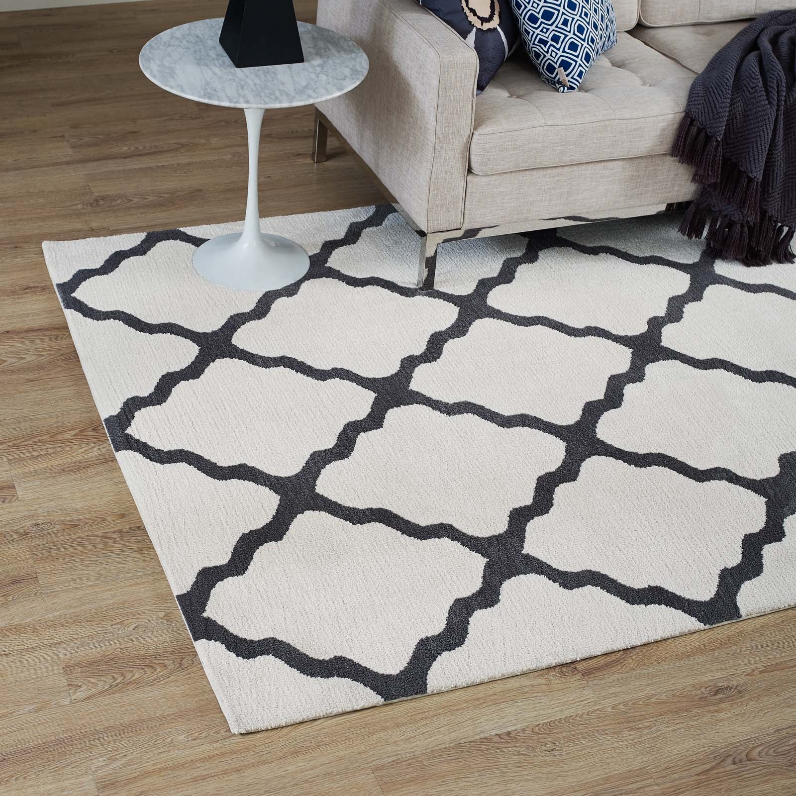 Ivory rug with bold dark gray lattice trellis, living room scene with beige sofa and round marble-topped side table.