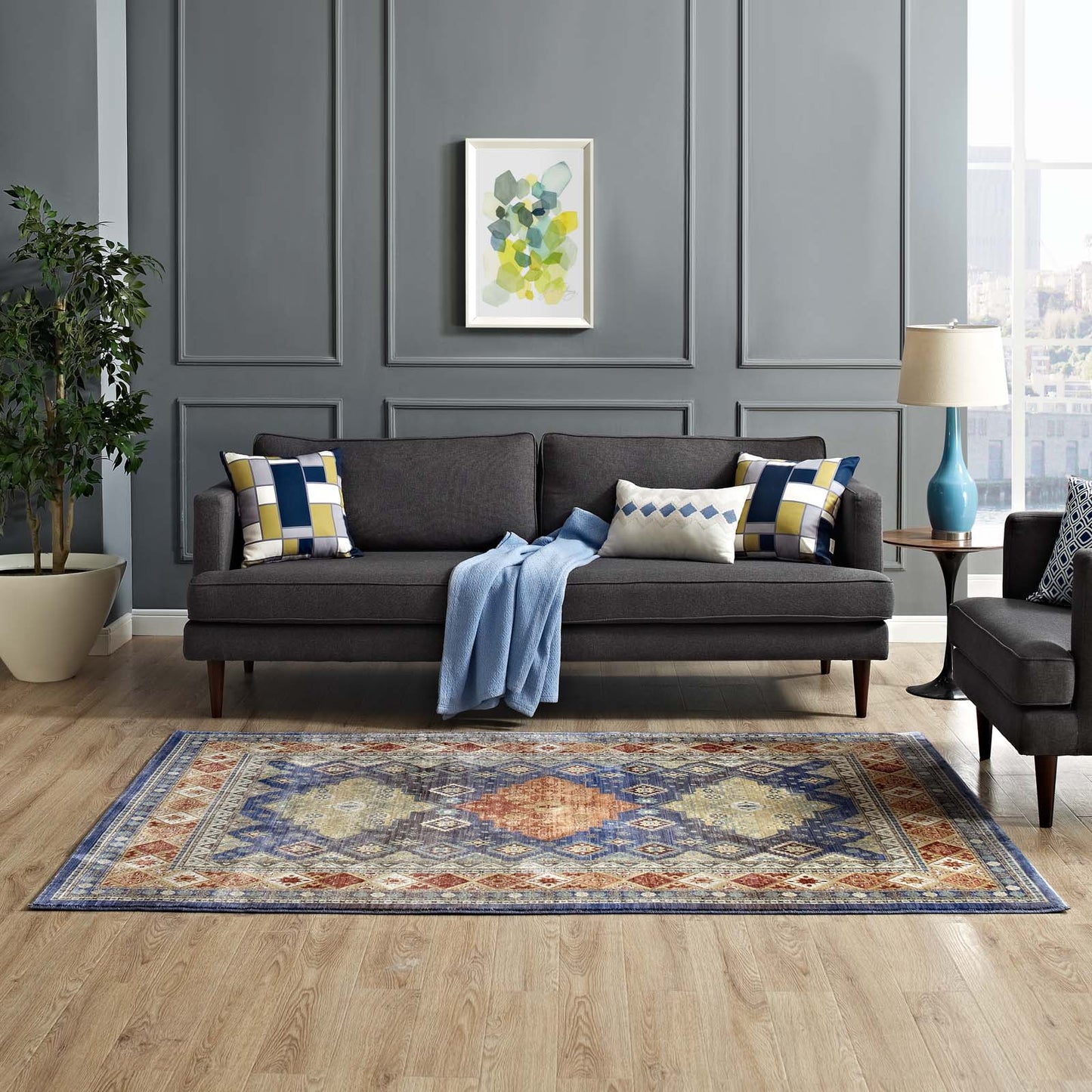 Multicolored distressed Southwestern diamond floral area rug in a paneled gray living room, with a dark gray fabric sofa, geometric cushions, and a blue throw.