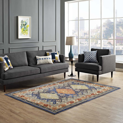 Modern living room with dark gray sofa and armchair, multicolored distressed southwestern diamond floral area rug, abstract wall art, large window, blue lamp.