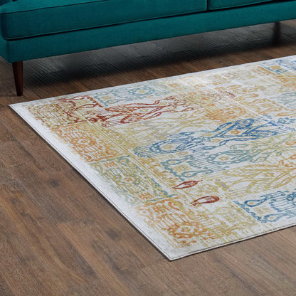 Colorful patterned area rug on wood floor, teal sofa in background; blue, yellow and red motifs.