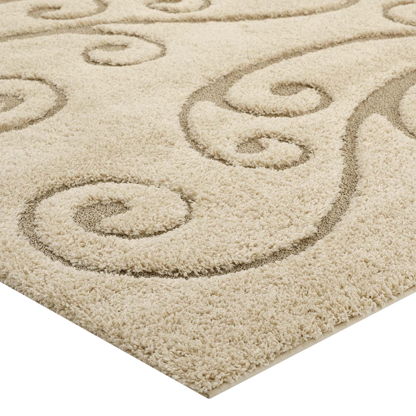 Beige plush area rug with dark decorative scroll-swirl pattern; thick soft pile and bound edge.