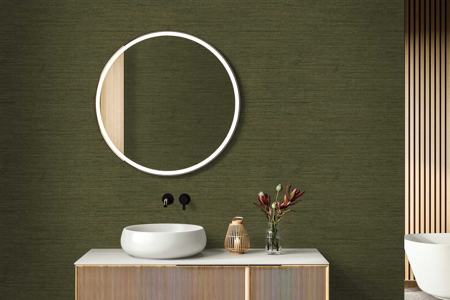 Round backlit mirror above white vessel sink on a wooden vanity, against a green faux-linen textured wall, with a vase of flowers.