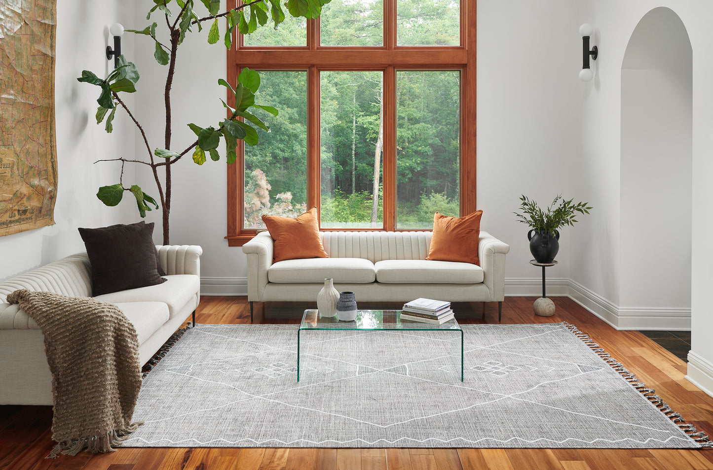 Gray patterned area rug under glass coffee table in a bright modern living room with white sofas and orange cushions.
