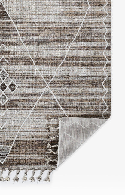 Grey woven rug with white geometric lines, diamonds and a zigzag border; fringe ends, folded corner shows lighter underside.