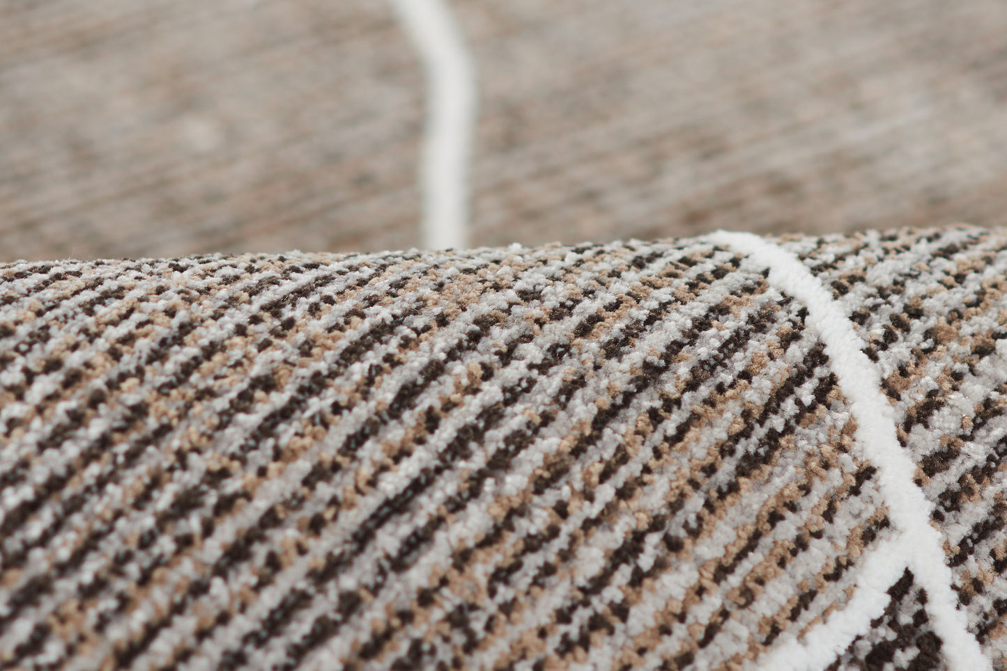 Close-up of a brown, beige and white striped woven rug with a white seam line.