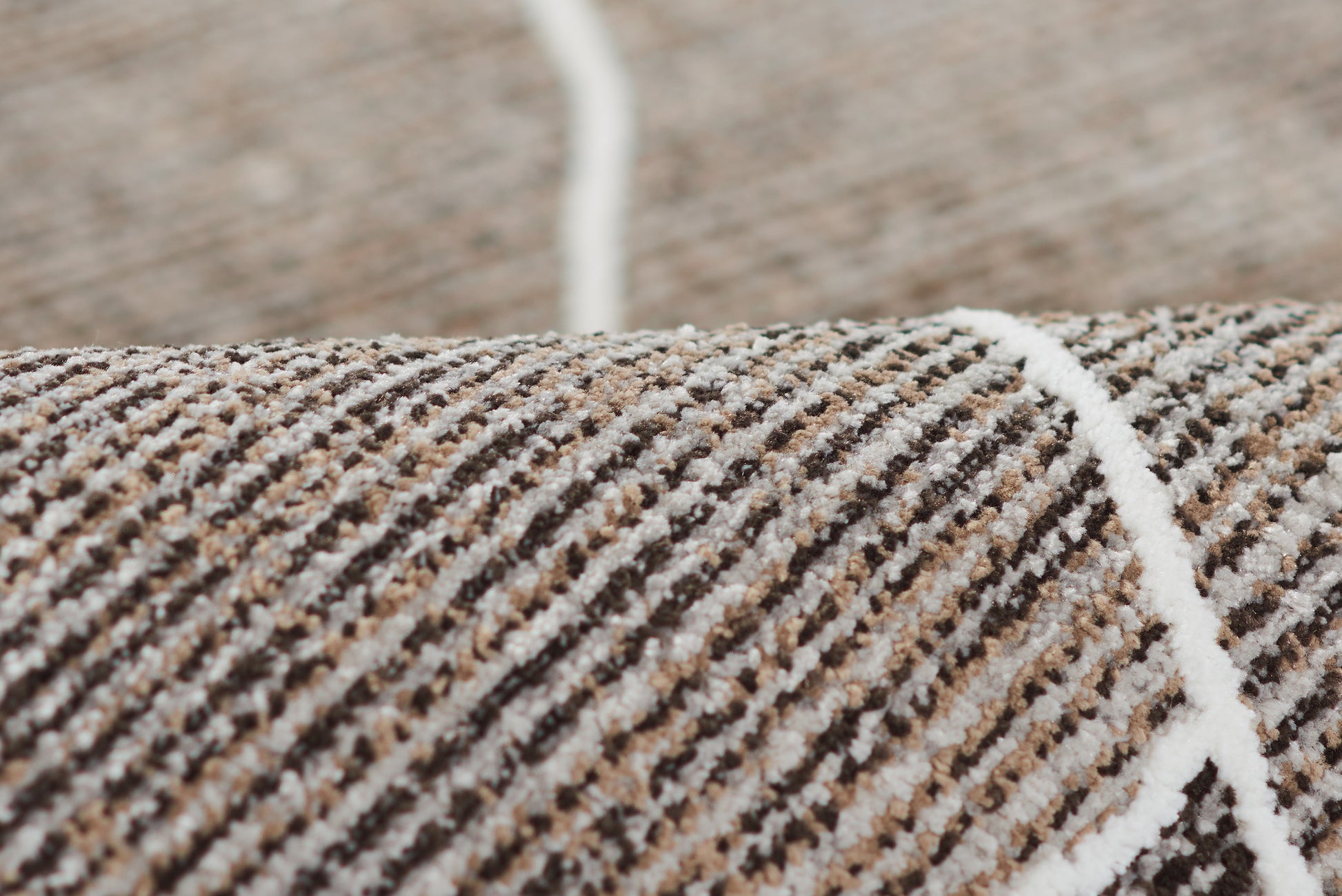 Close-up of a brown, beige and white striped woven rug with a white seam line.