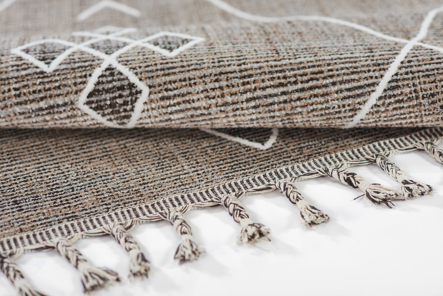 Gray woven rug with white geometric pattern, folded edge and fringe tassels.