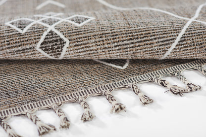 Gray woven rug with white geometric pattern, folded edge and fringe tassels.