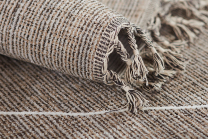 Beige and gray striped woven rug with tassel fringe along the edge, rolled at the corner.