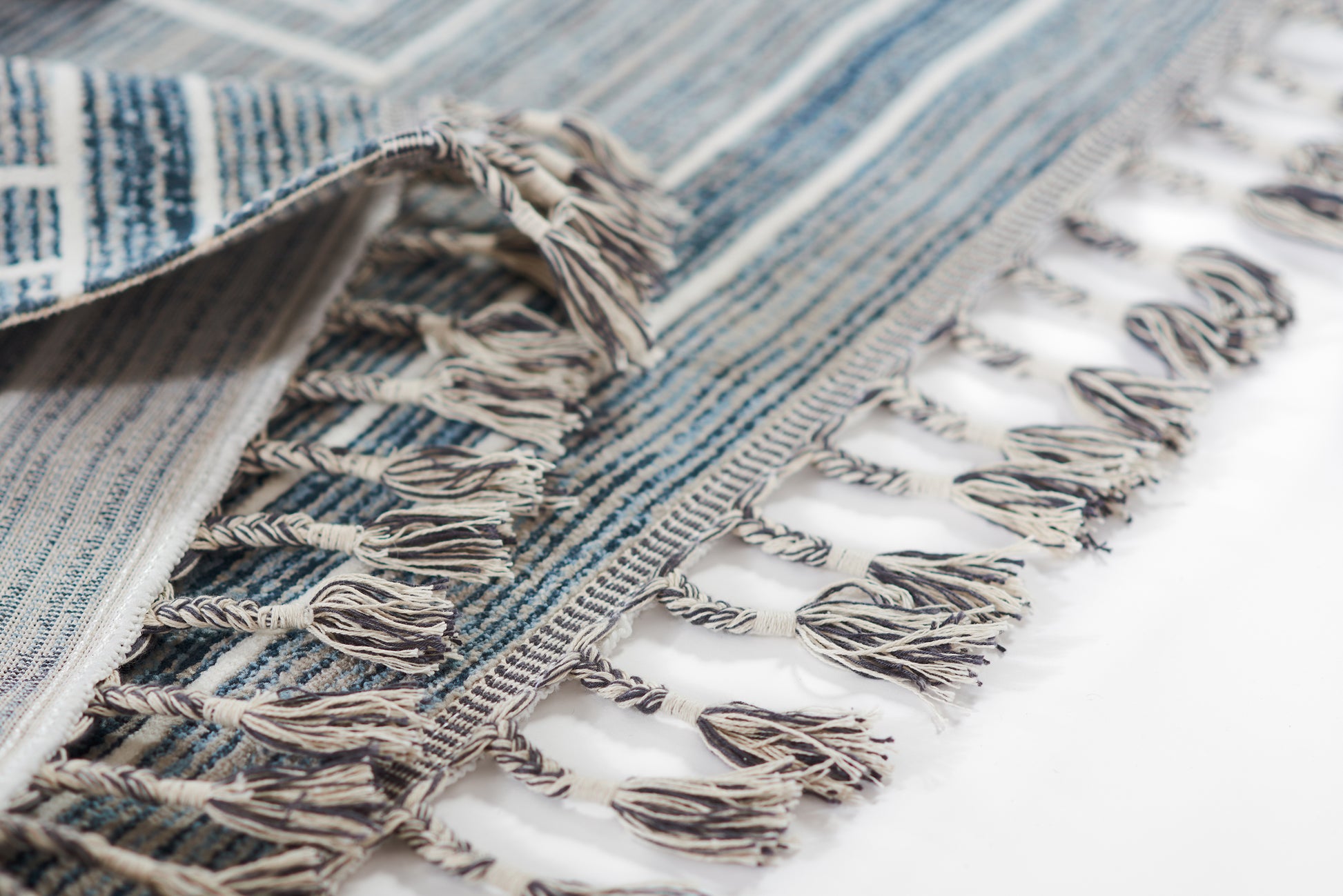 Blue and white striped woven cotton rug with fringed tassels along edges.